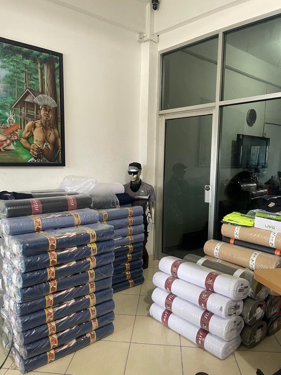 Tumpukan gulungan bahan kain biru, putih, dan krem di ruang produksi
