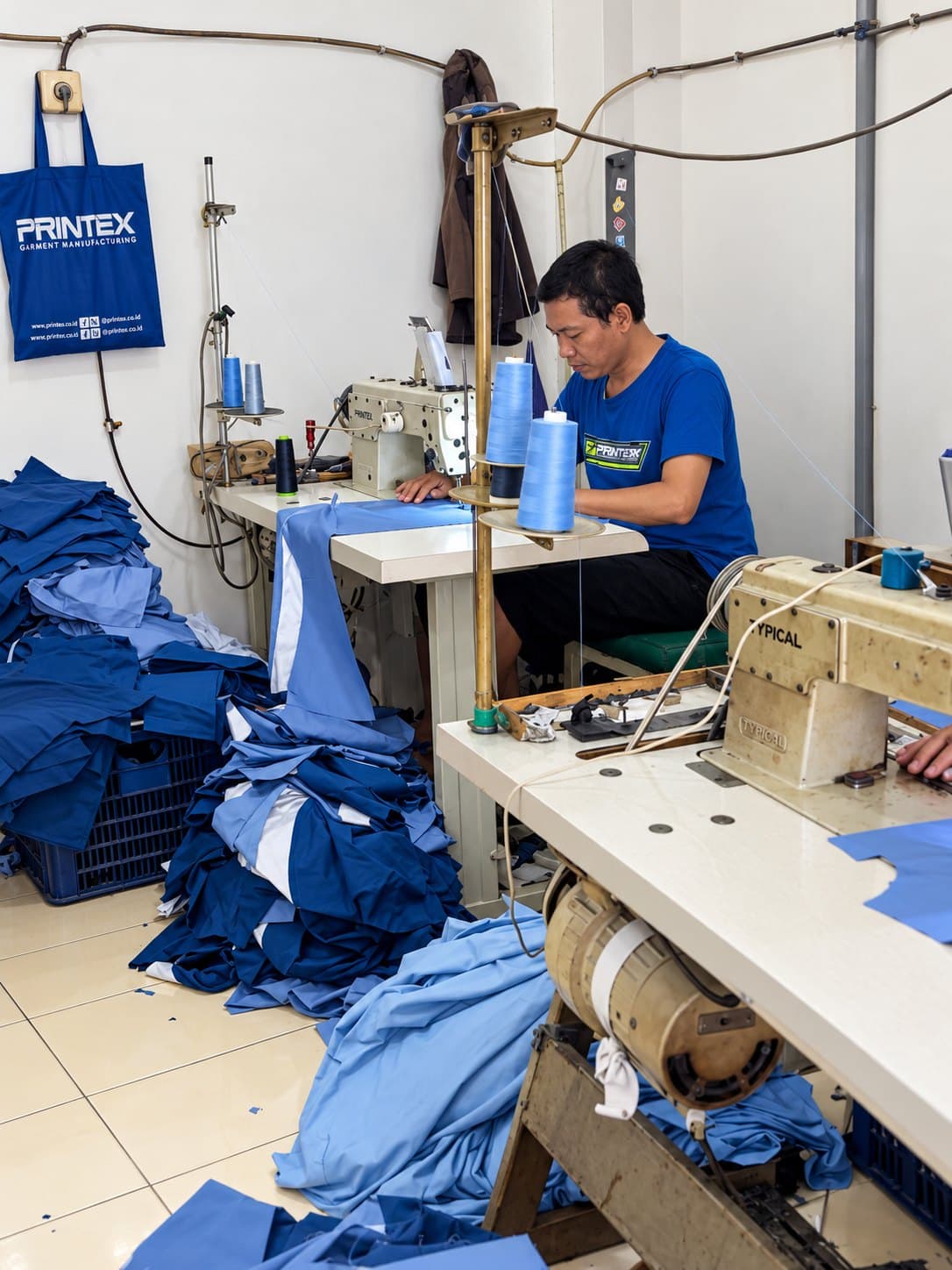 Penjahit bekerja di mesin jahit dengan tumpukan potongan kemeja biru
