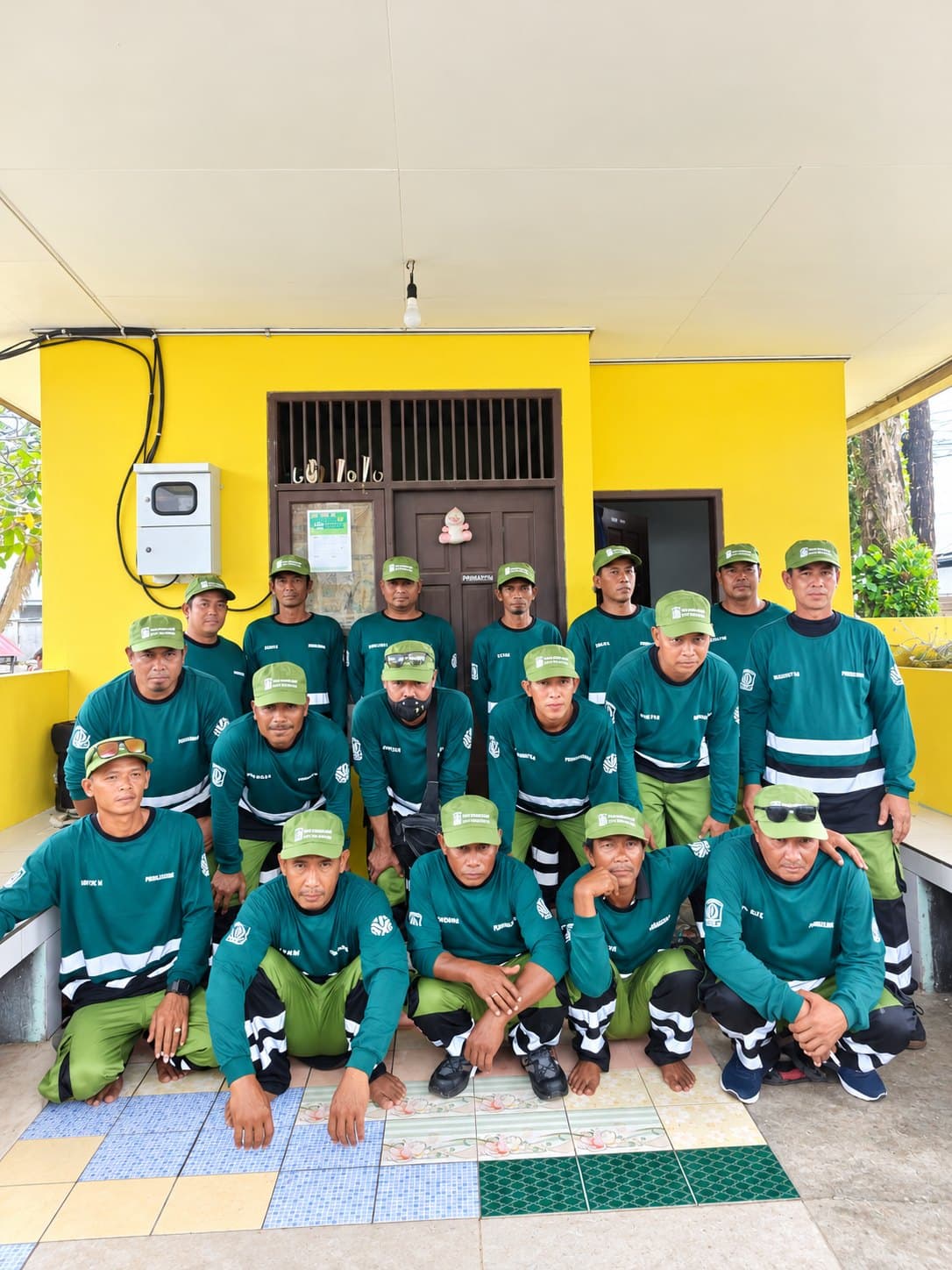 Tim lapangan berfoto bersama memakai seragam hijau lengan panjang dengan list reflektif dan topi