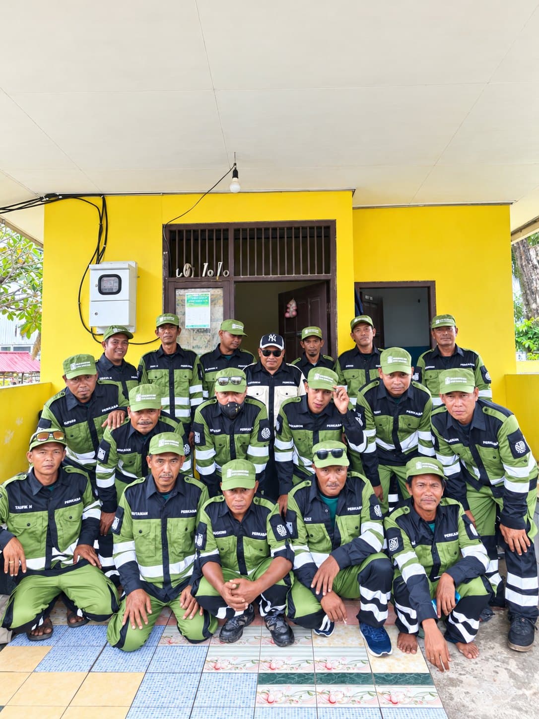 Tim lapangan memakai seragam hijau dan hitam dengan list reflektif, berfoto bersama